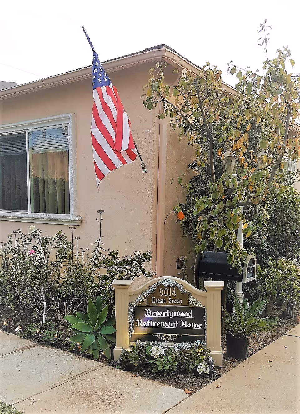 Exterior view of Beverlywood Retirement Home with American flag and garden.