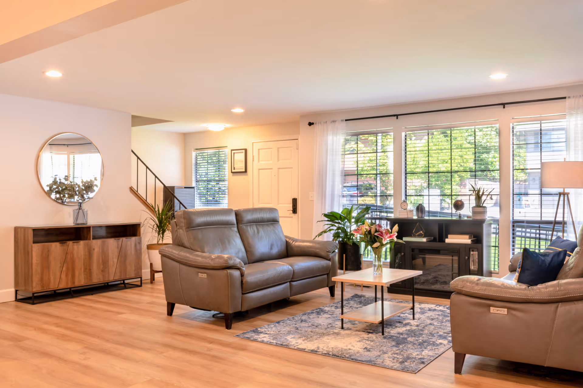 Well lit senior living room with leather sofas, coffee table, plants, and large windows.