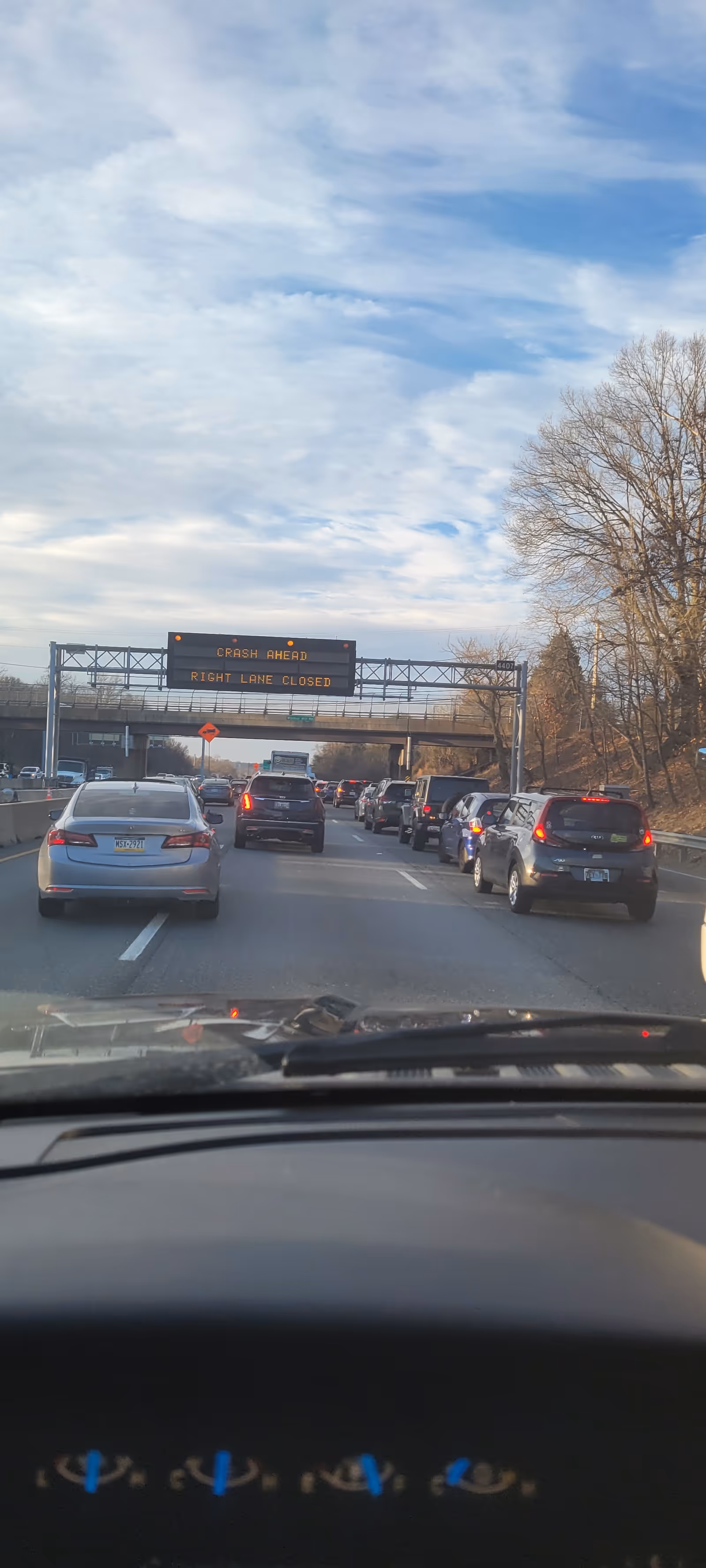 View from a car on a highway with overhead sign: CRASH AHEAD, RIGHT LANE CLOSED.