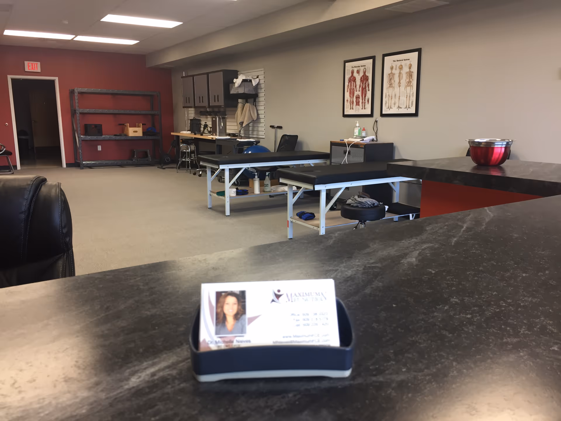 A clinical therapy room with treatment tables, medical posters, and a front counter.