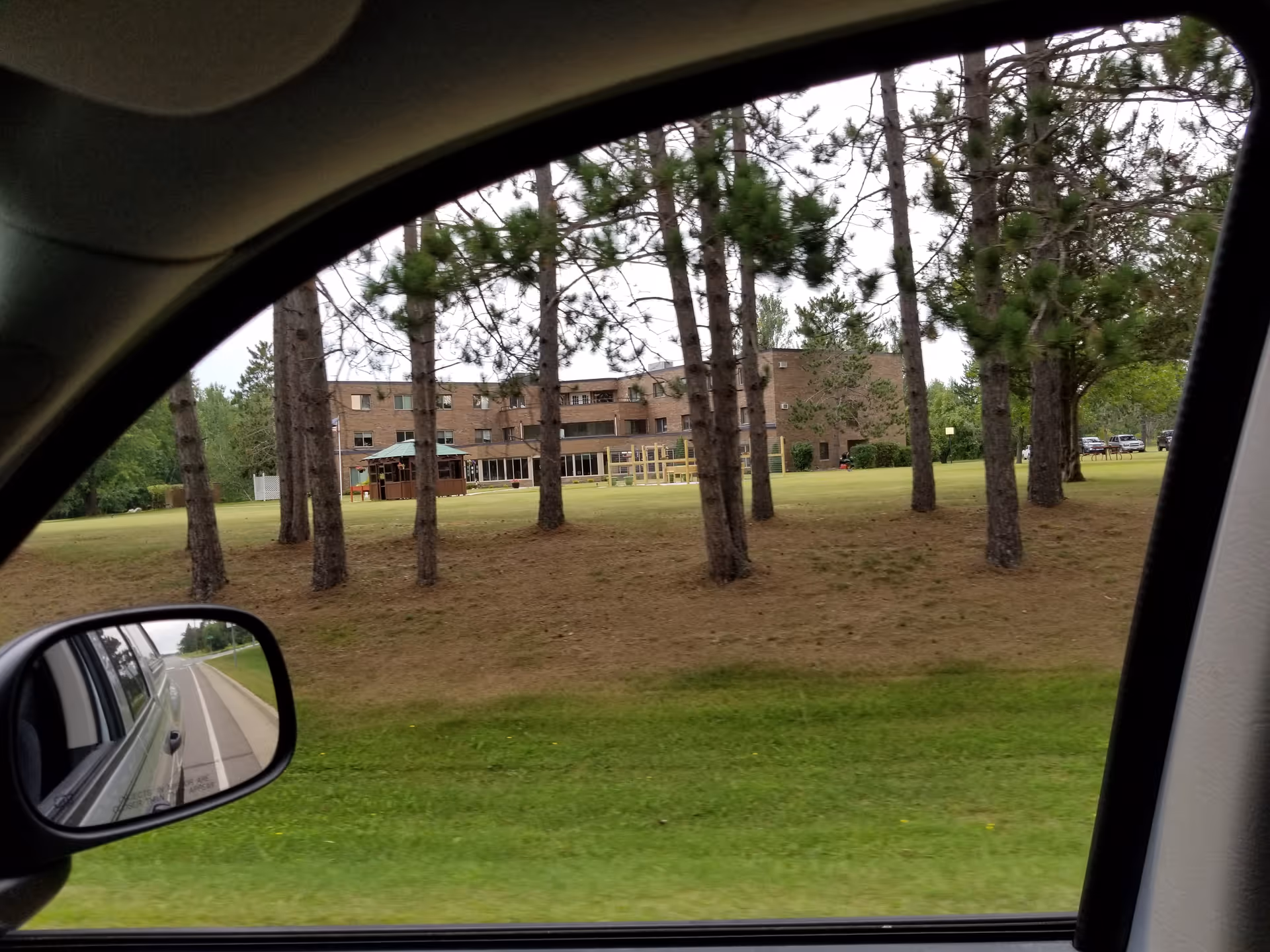 Exterior view from a car of a building with trees and a grassy lawn.
