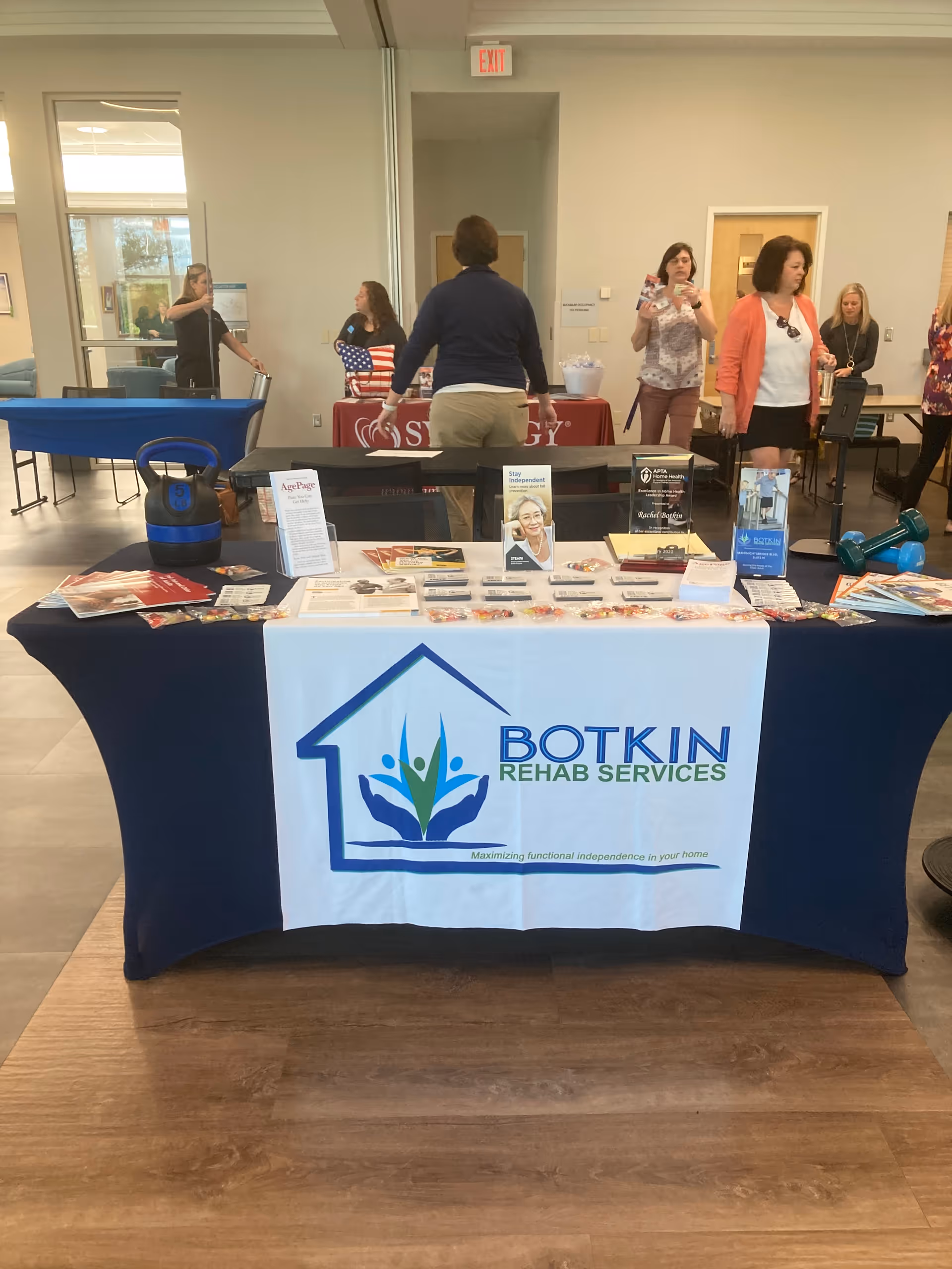 Indoor lobby scene featuring a Botkin Rehab Services promotional table and visitors.