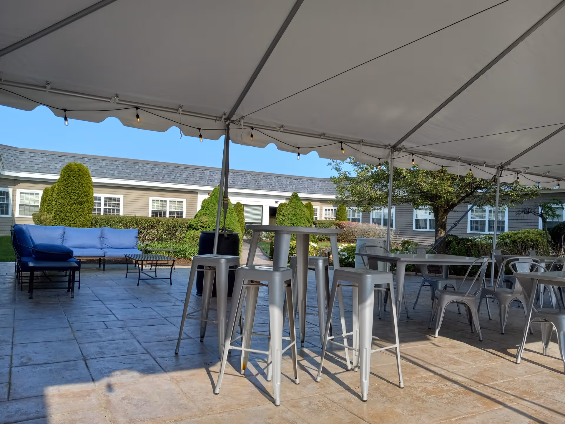Outdoor patio at Alden Court Nursing Care with high tables, metal chairs, and blue cushioned seating.