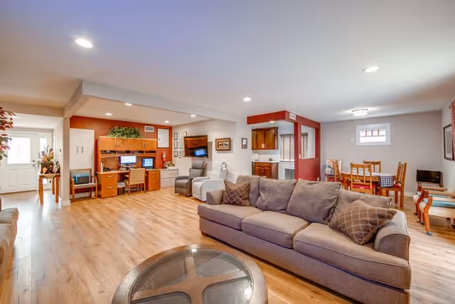 Spacious communal living area with sofas, a coffee table, computer workstations, and a dining table.
