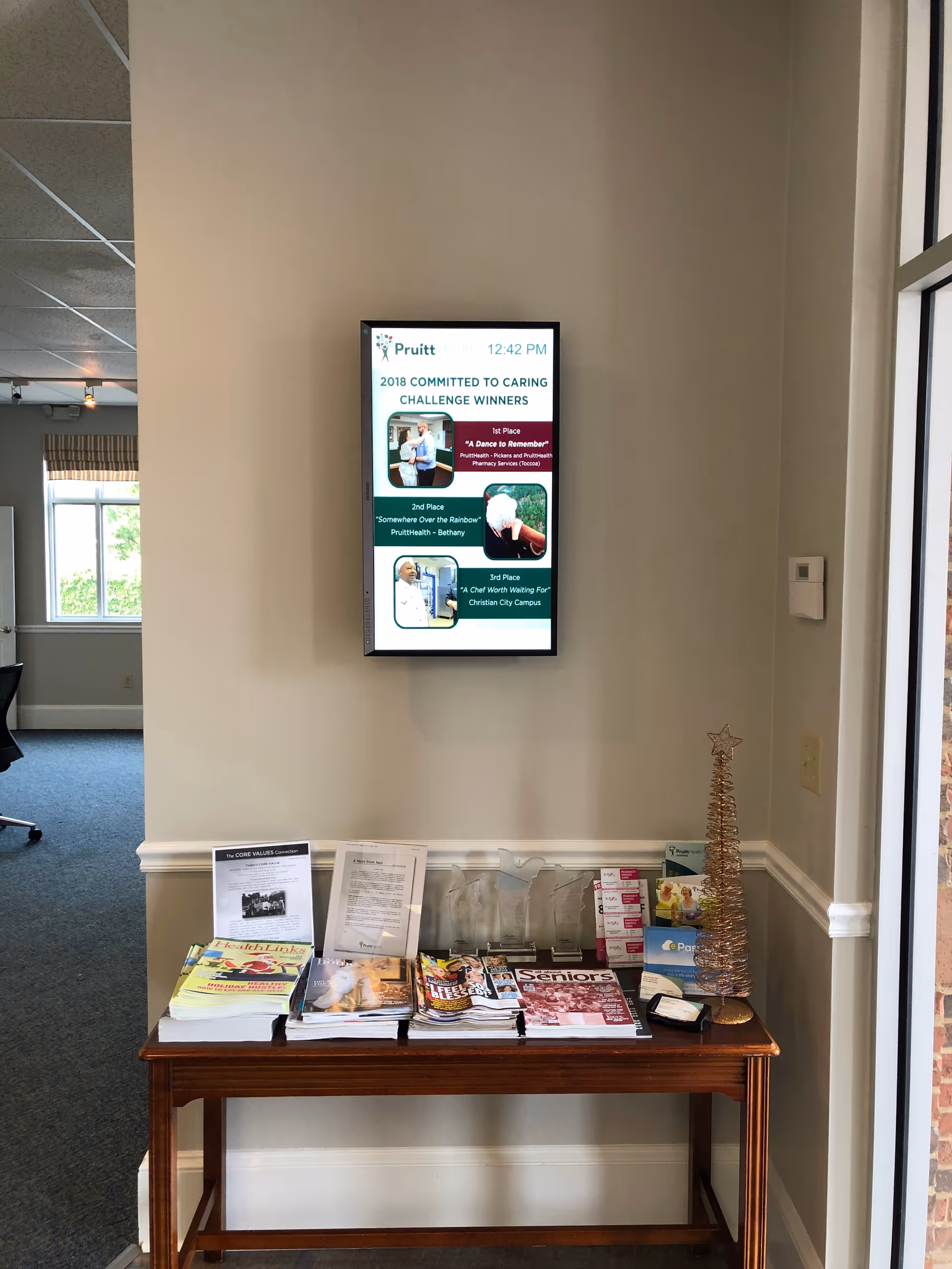 Interior lobby area with wall-mounted digital display and brochure table beside a small Christmas tree.