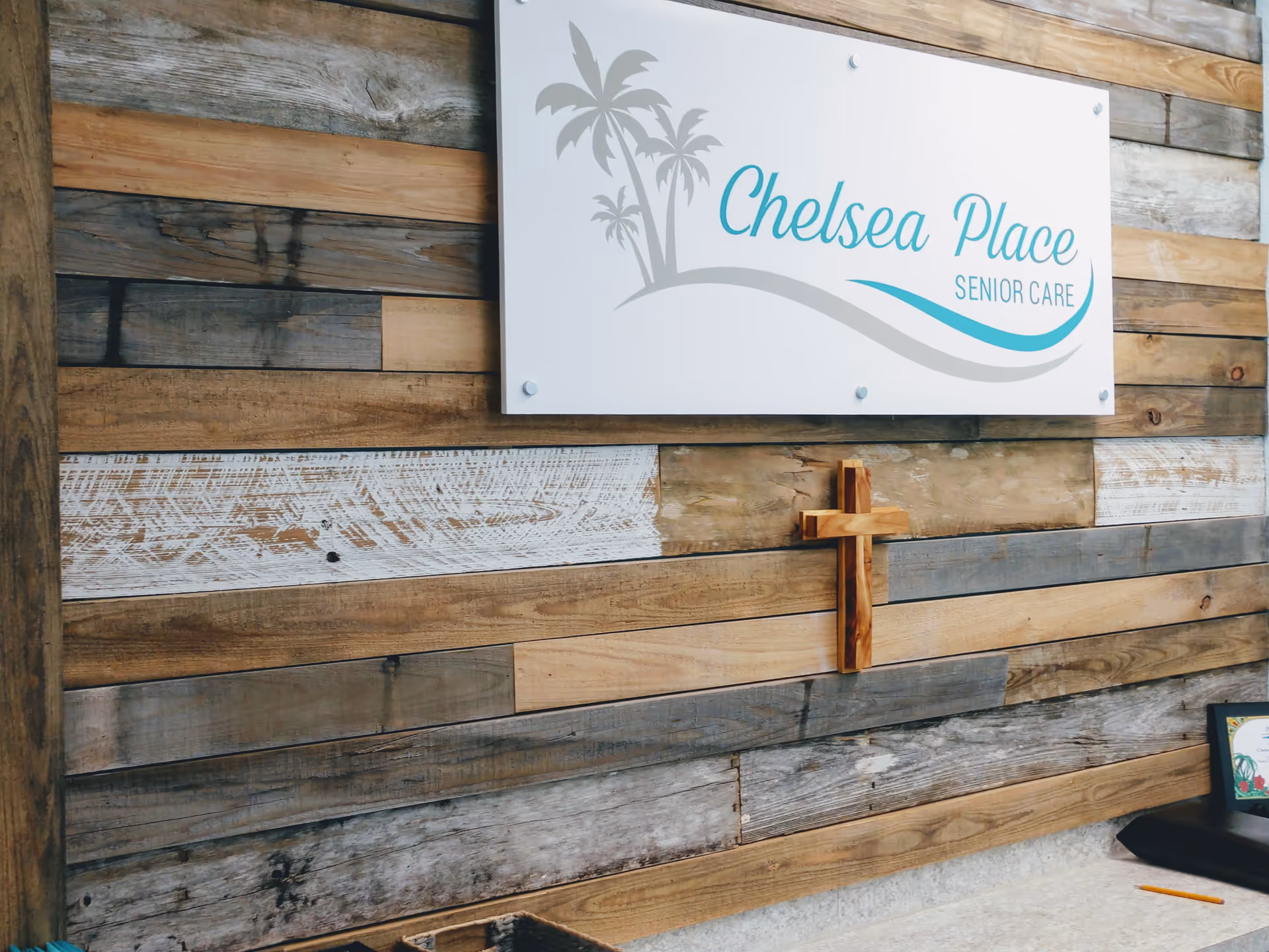 Exterior wooden wall with Chelsea Place Senior Care sign and a wooden cross.