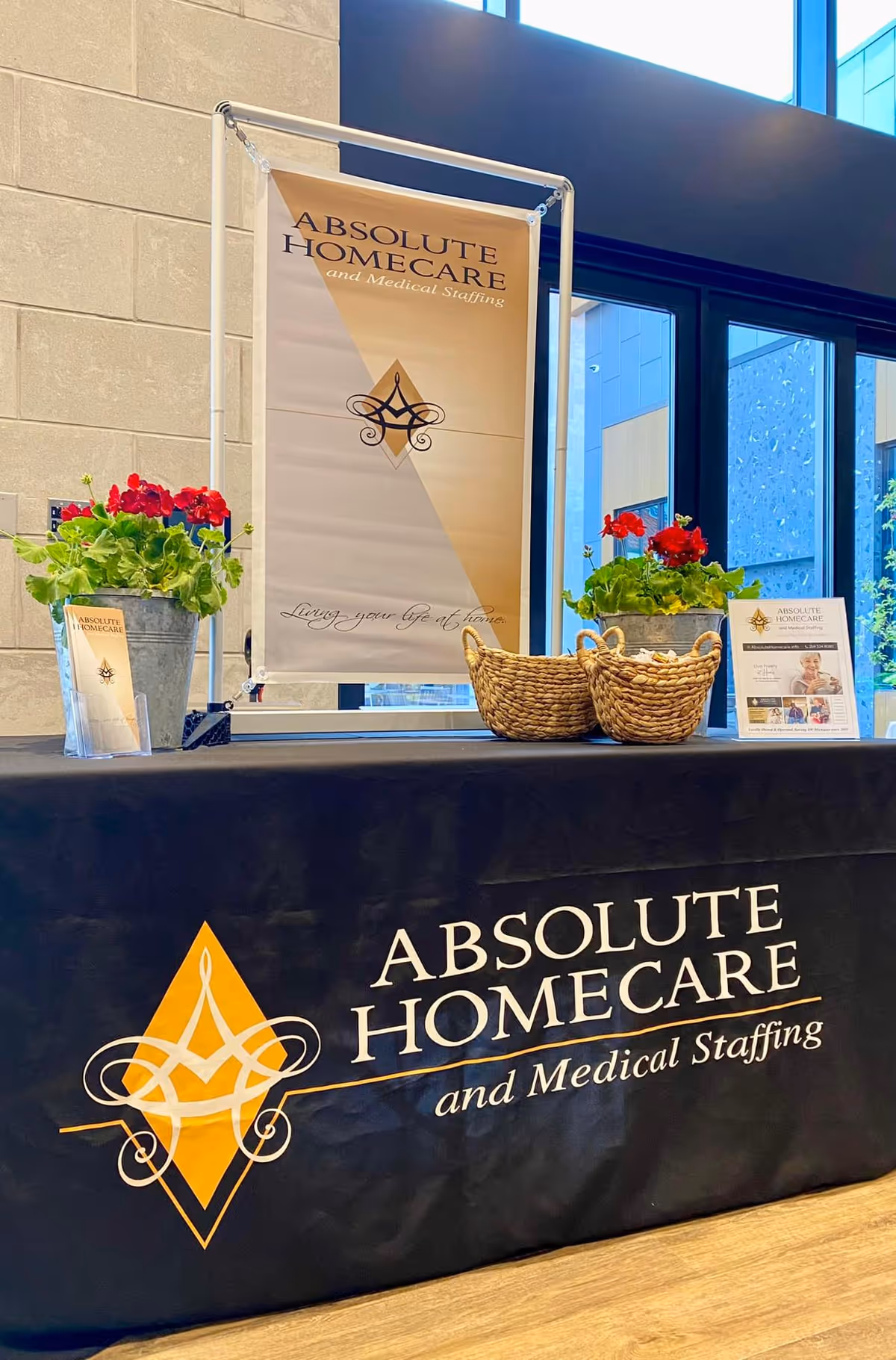 Registration table with Absolute Homecare banner and potted plants in a lobby