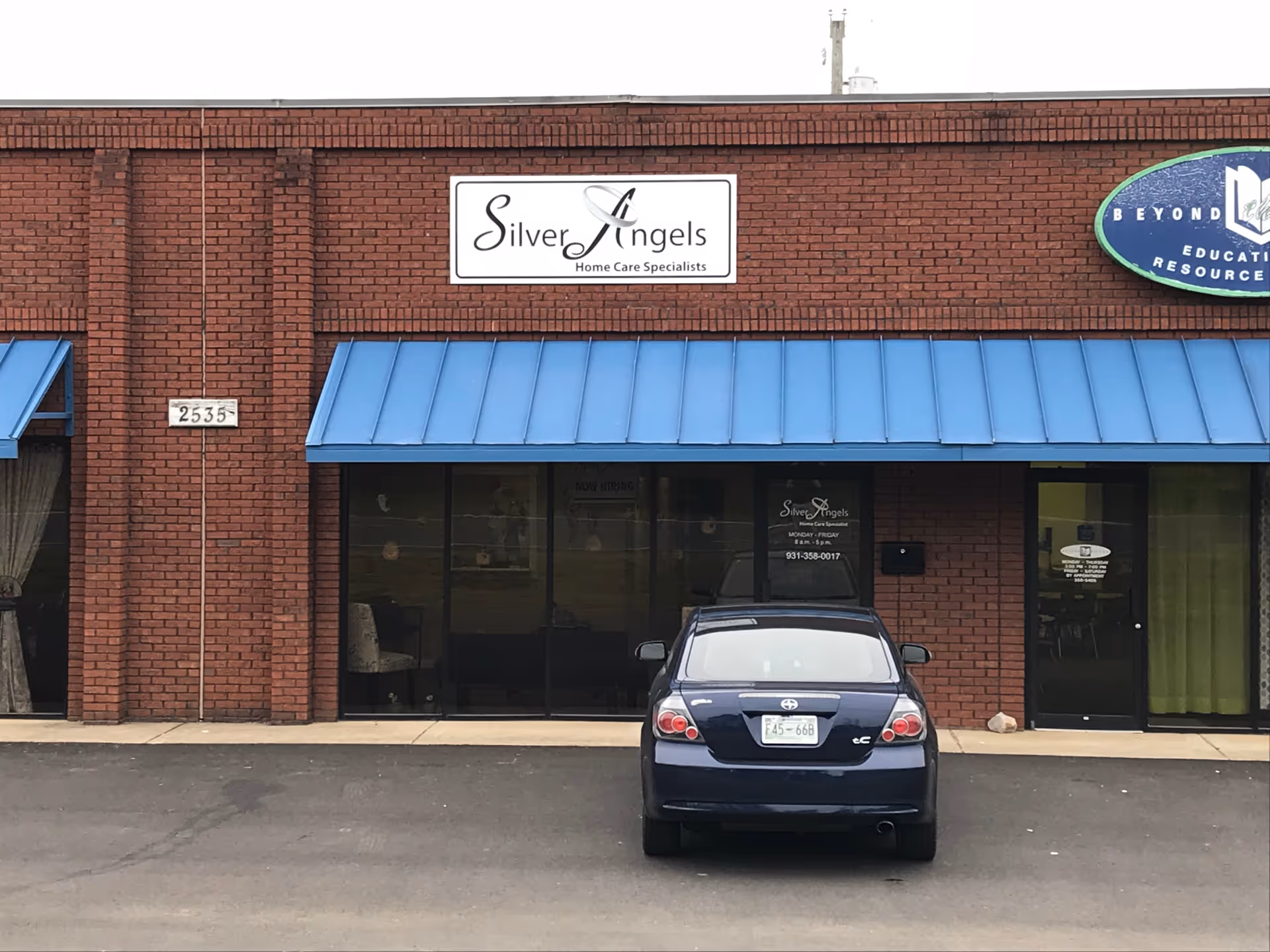 Brick storefront with blue awning and a car parked in front of Silver Angels.