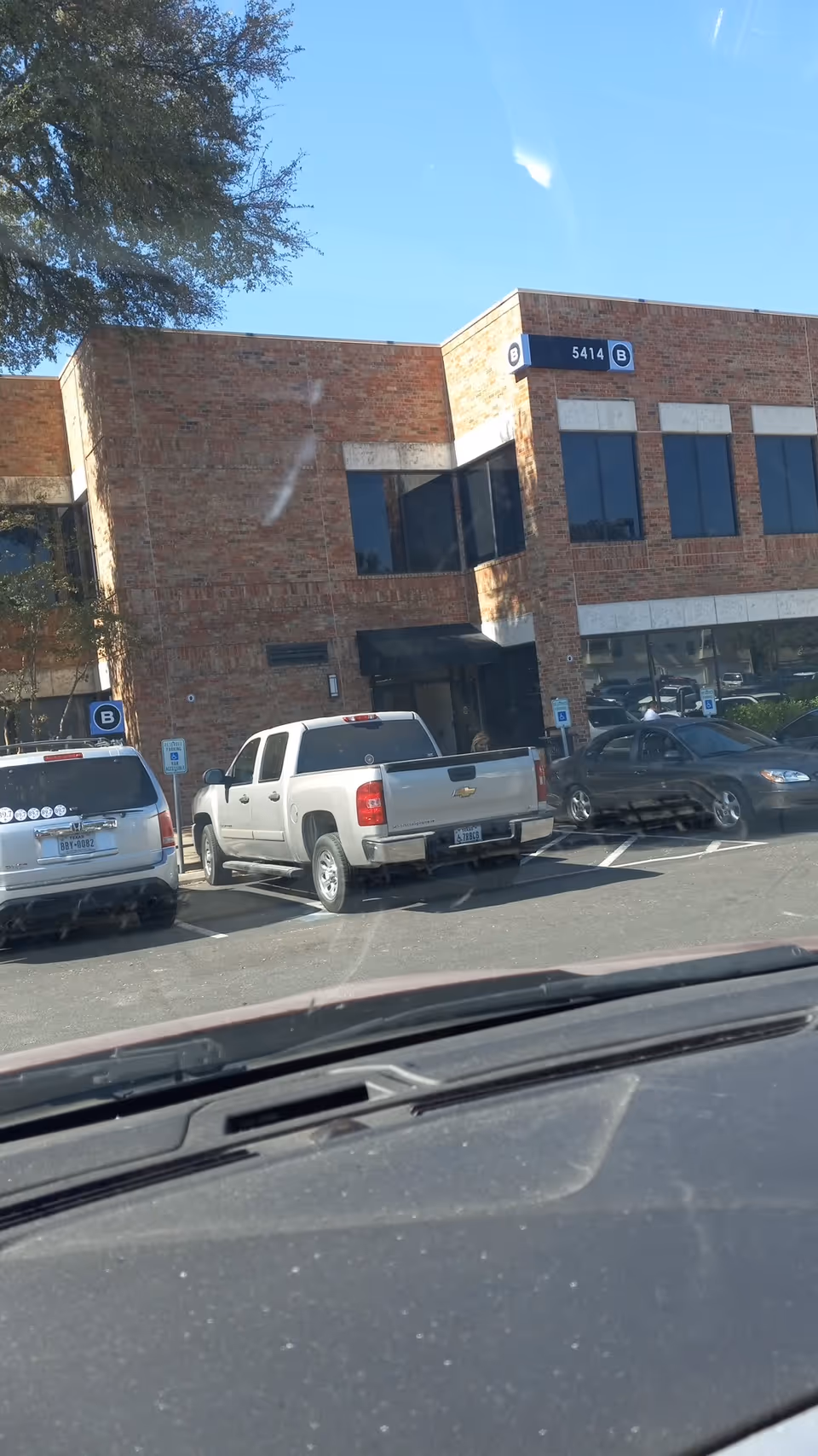 Brick office building with windows and several parked cars in front.