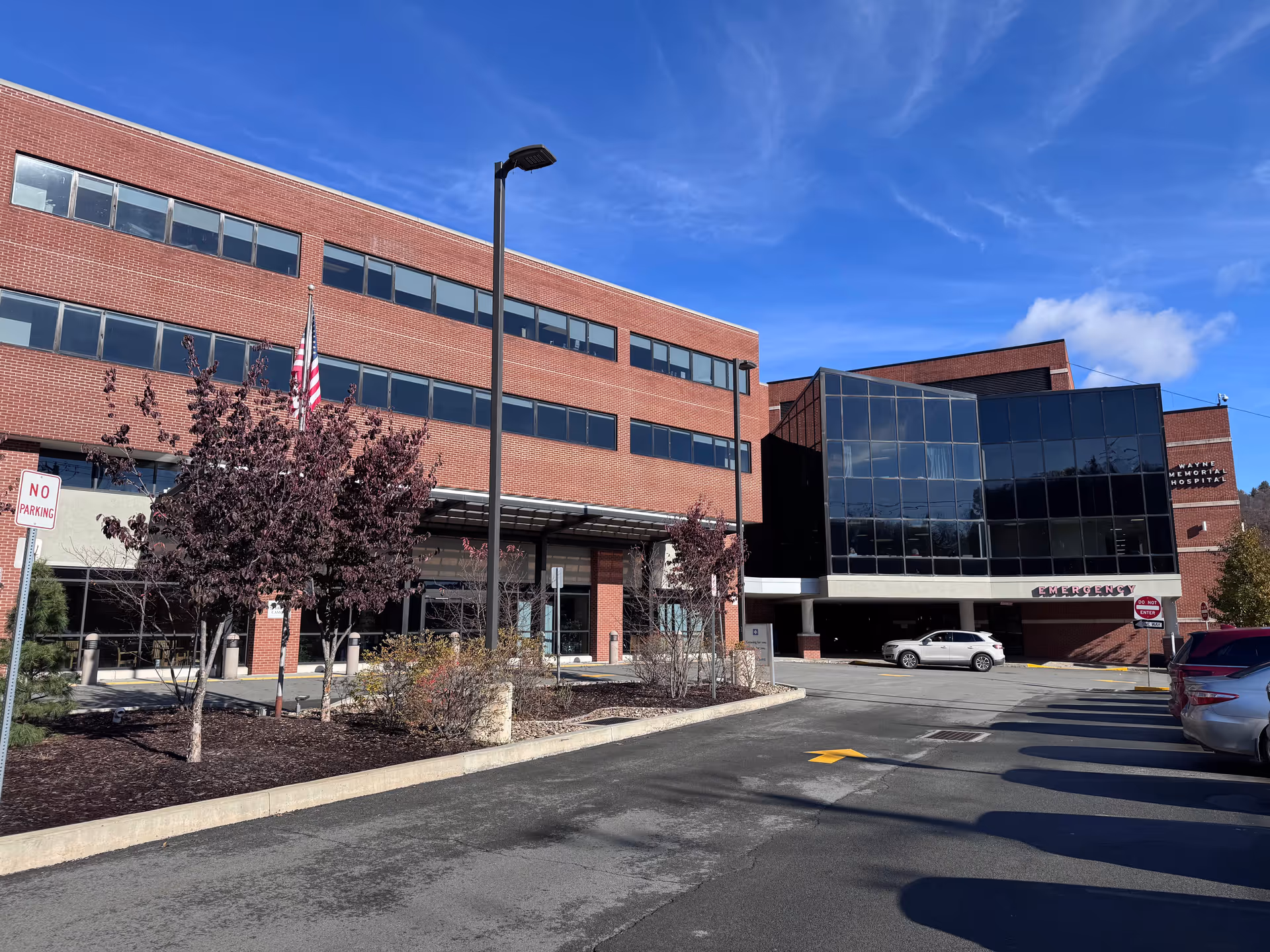 Exterior view of Wayne Memorial Hospital with brick facade, glass entrance, and parked cars.