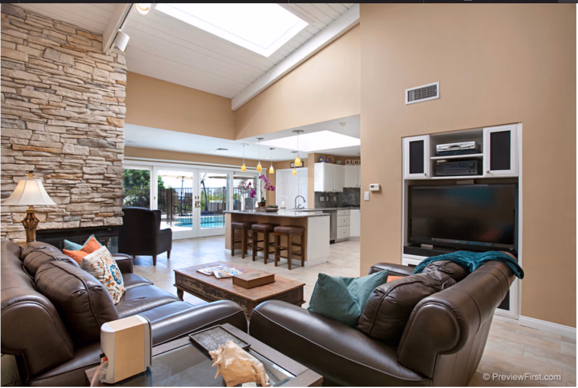 Open-concept living room with leather sofas, stone accent wall, and a kitchen island.