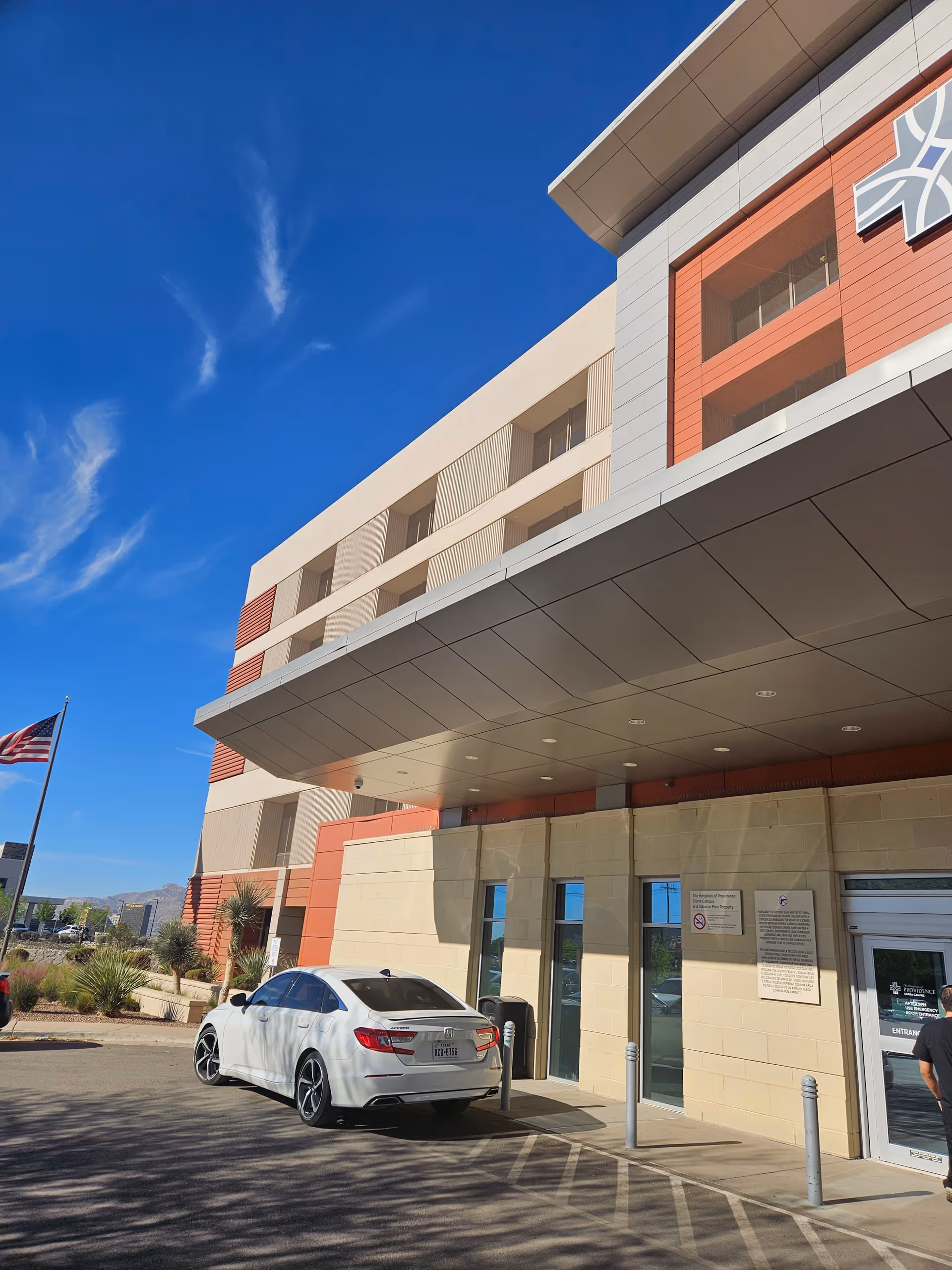 Exterior view of Sierra Providence Total Care with entrance canopy, parked car, flag, and blue sky.