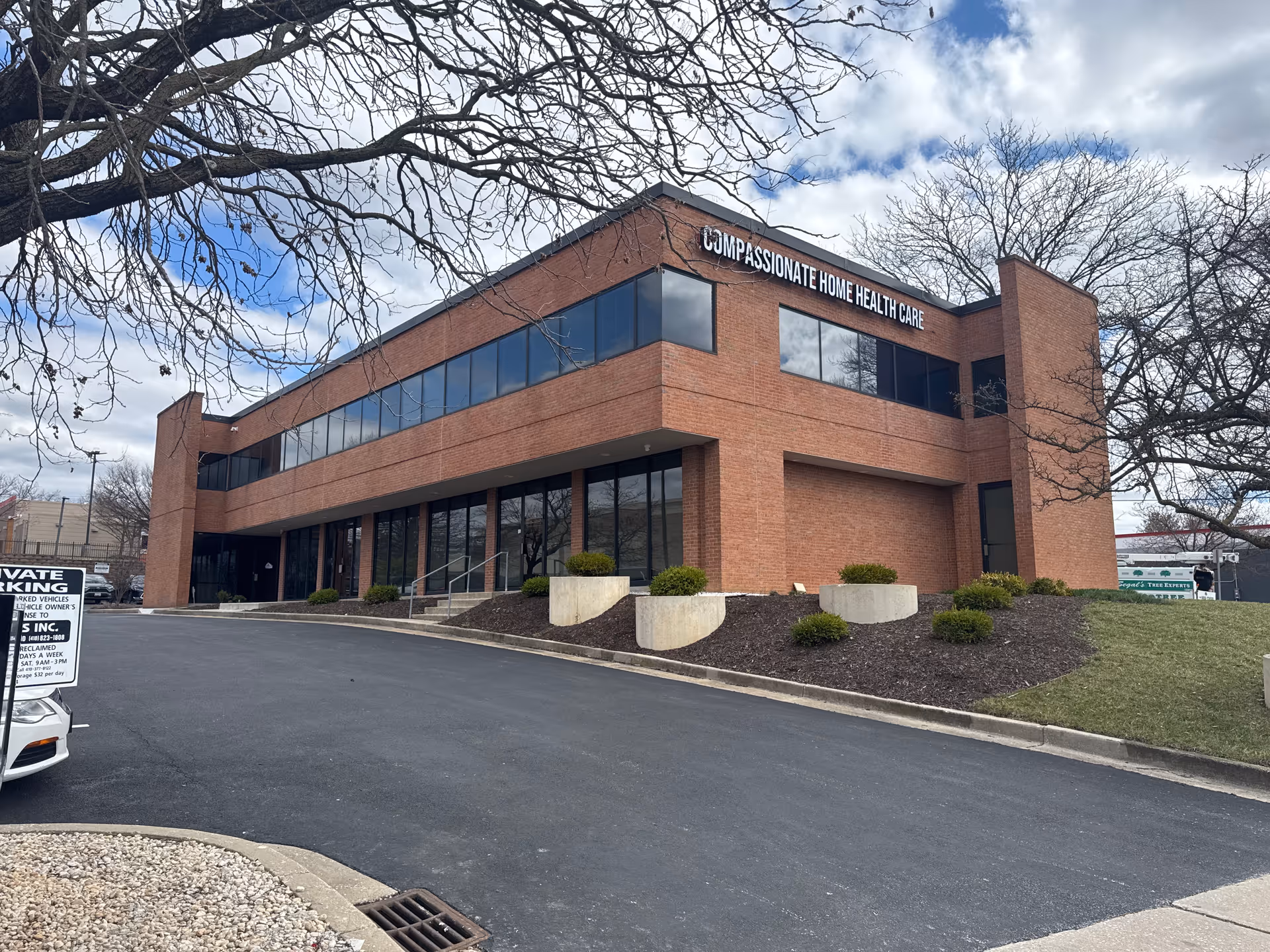 Brick two-story building labeled Compassionate Home Health Care with parking lot and bare trees.
