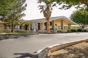 Front exterior of a single-story senior living facility with curved driveway and palm trees.