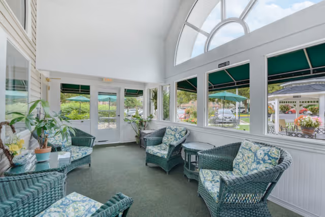 Sunlit enclosed seating area in Cascades Village, with wicker chairs, plants, and arched windows.