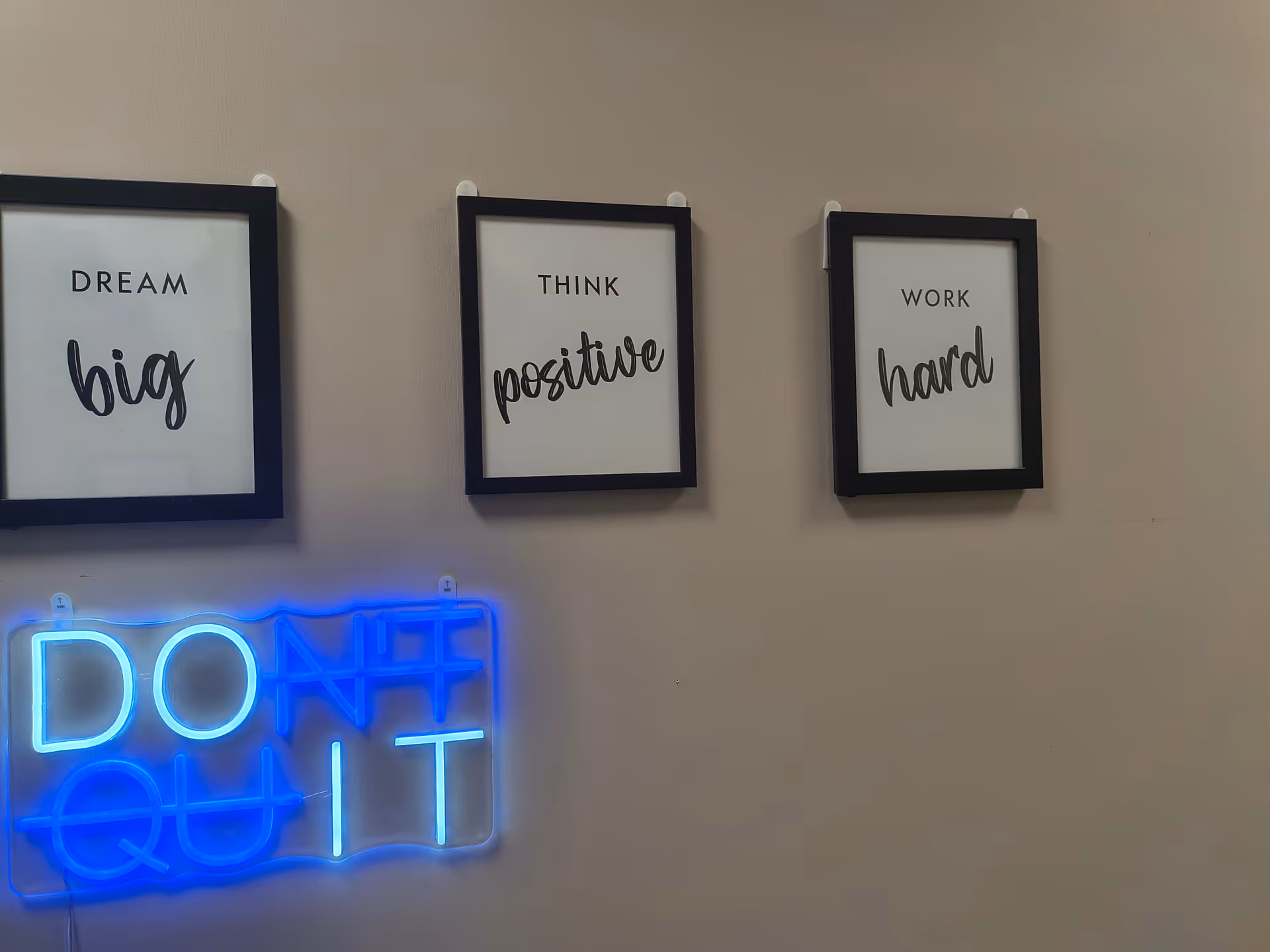 Three framed quotes on a wall: Dream big, Think positive, Work hard; blue neon DONT QUIT.