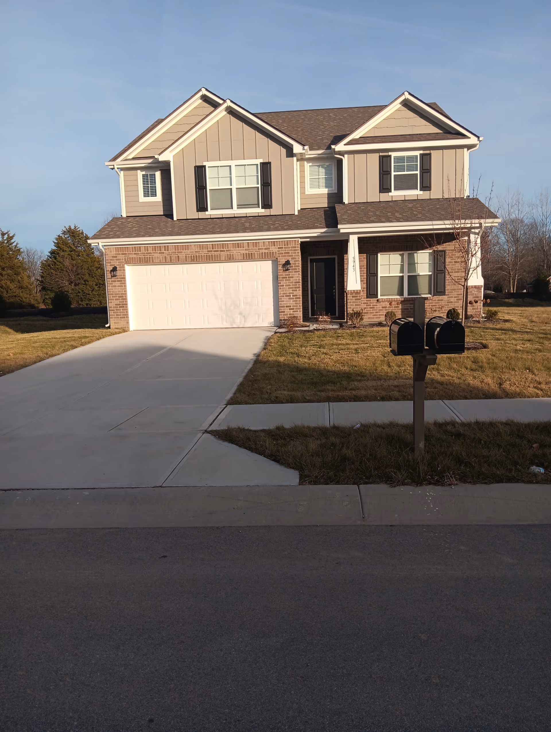 Two-story suburban house with brick lower facade, attached garage, and mailbox at curb.