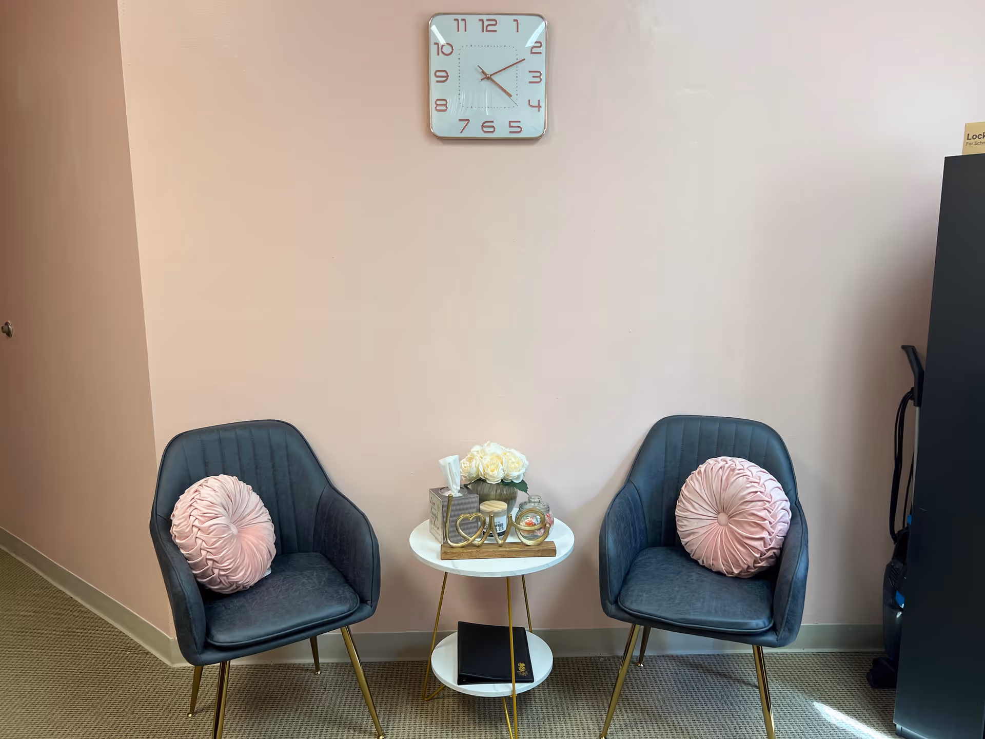 Two blue armchairs with pink cushions flank a small white table in a pastel lounge.