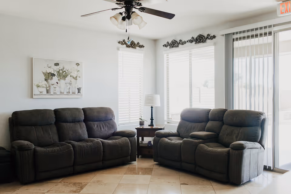 Cozy indoor living room with two recliner sofas, a side table, and windows.