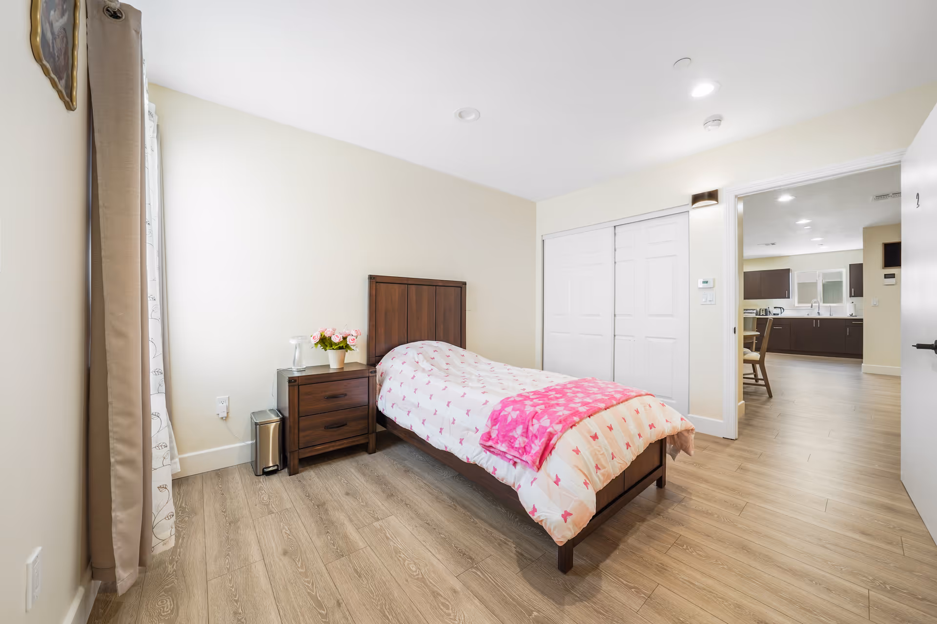 A tidy bedroom with a wooden bed, nightstand, and pink-accented quilt.