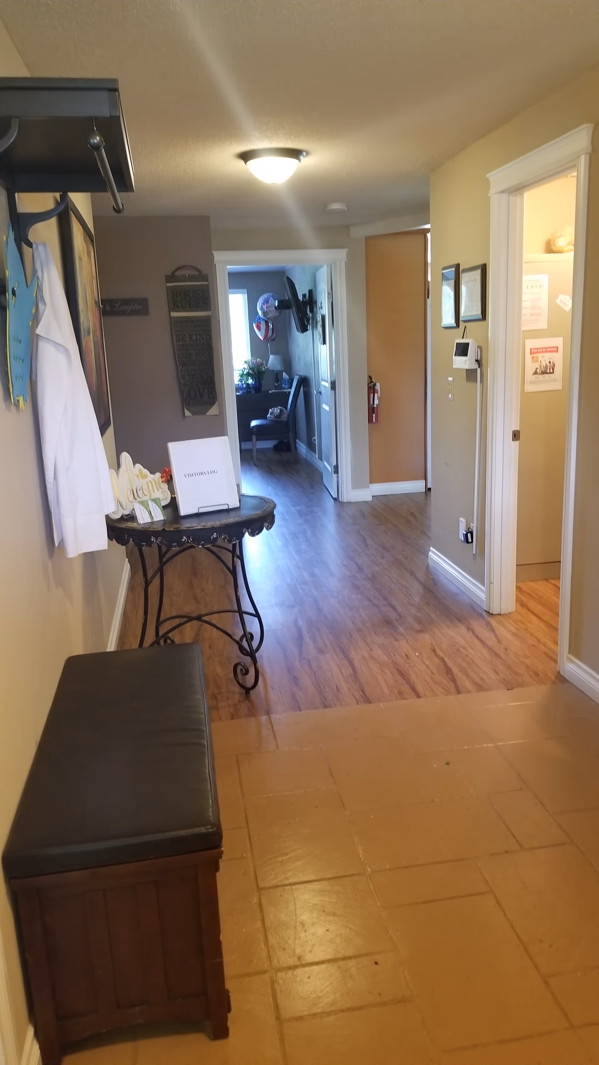 Interior hallway of a senior living facility featuring a bench, table, coats, and multiple doorways.