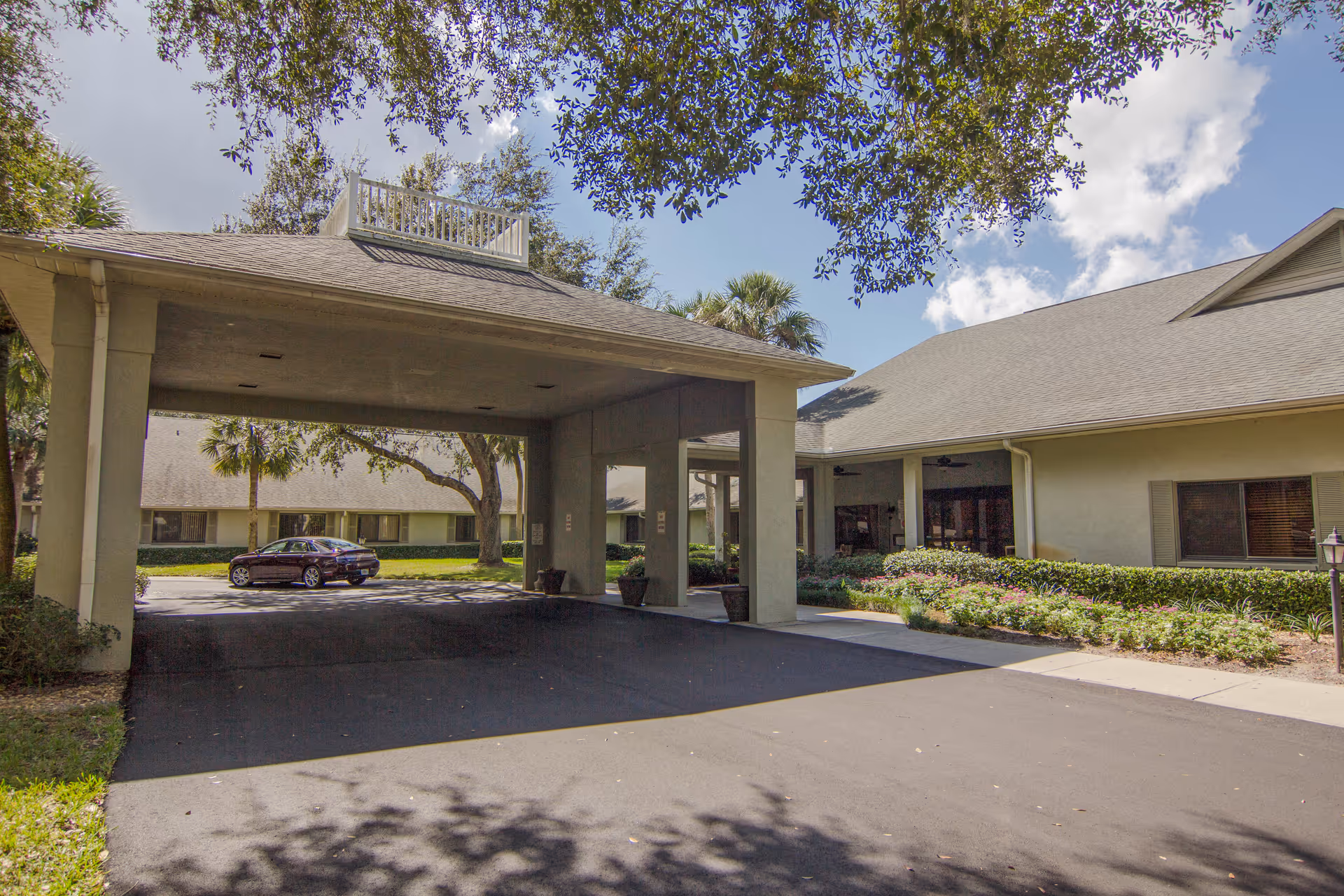 Exterior view of a senior living facility entrance with a covered driveway and surrounding landscaping.