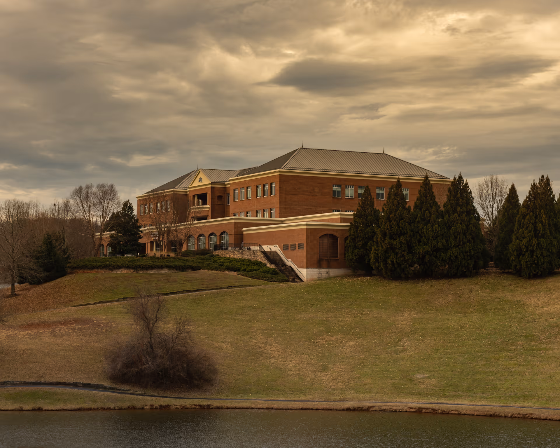 A brick senior living facility sits on a grassy hill by a lake.