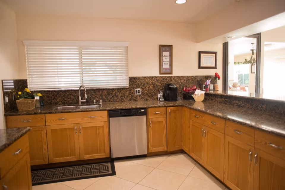L-shaped kitchen with granite countertops, wooden cabinets, sink, and dishwasher.