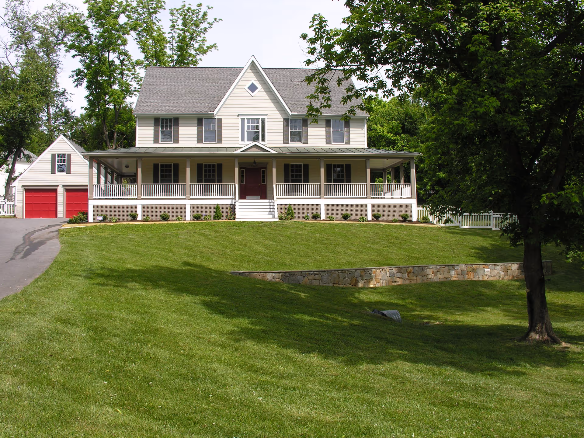 Two-story house with a wide front porch, red double garage, and a large green lawn.