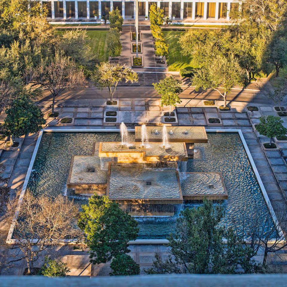 Aerial view of a rectangular fountain plaza with water features, trees, and walkways.
