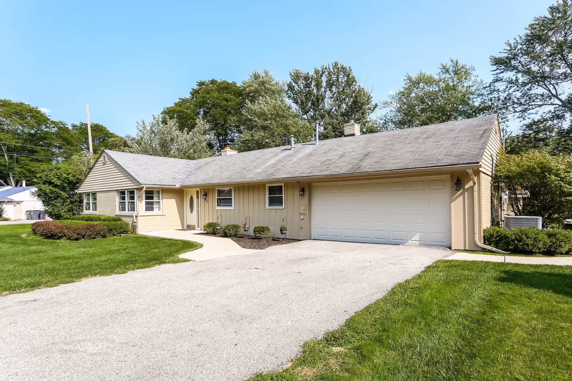 Single-story beige assisted living home with attached two-car garage and green lawn.