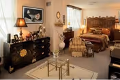 A warmly lit bedroom with two ornate beds, dressers, lamps, and vintage decor.