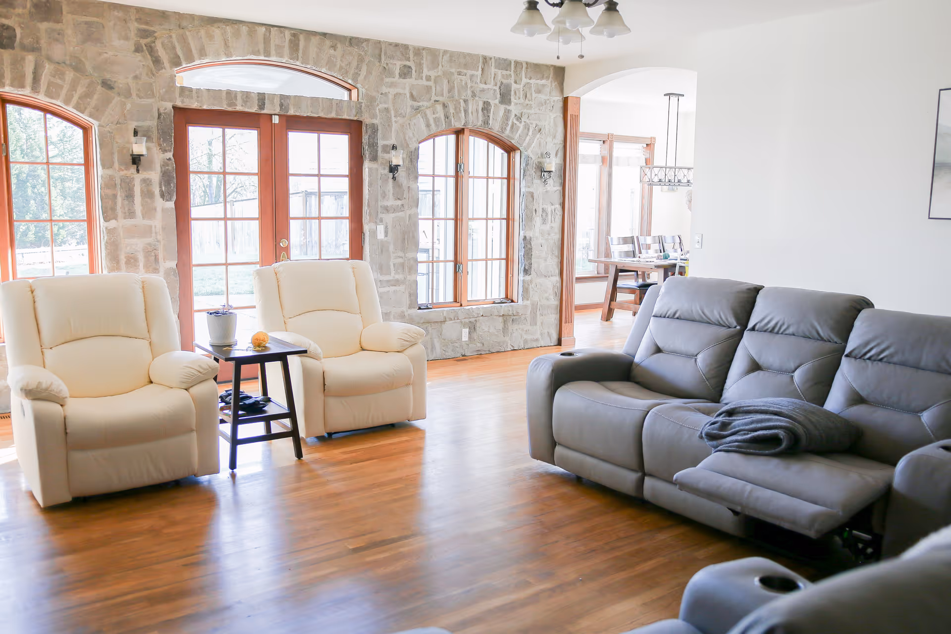 Stone-walled living room with beige recliners, gray sofa, and wooden floors.
