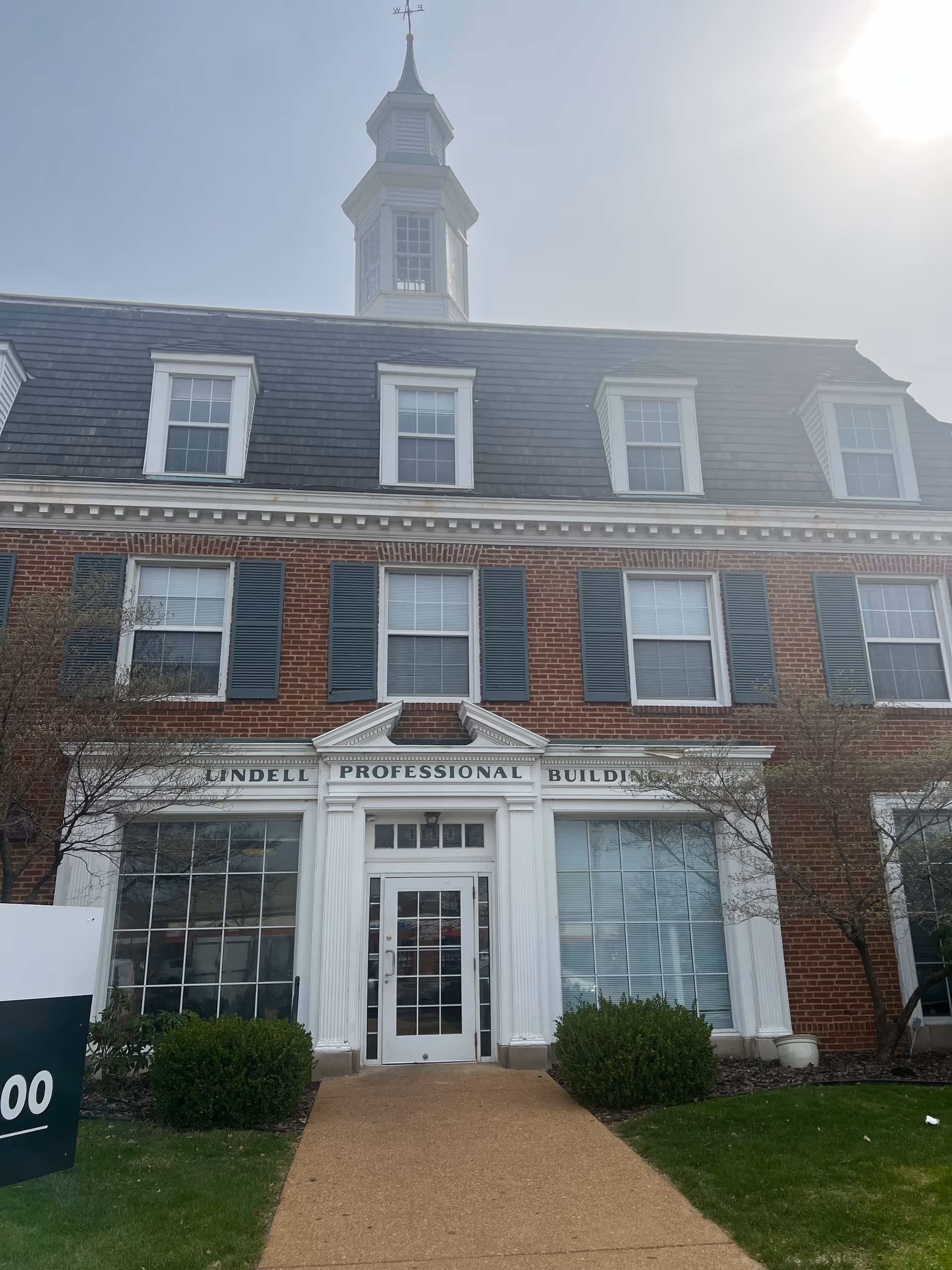Brick professional building facade with white columns, multiple windows, and a pitched roof with a cupola.