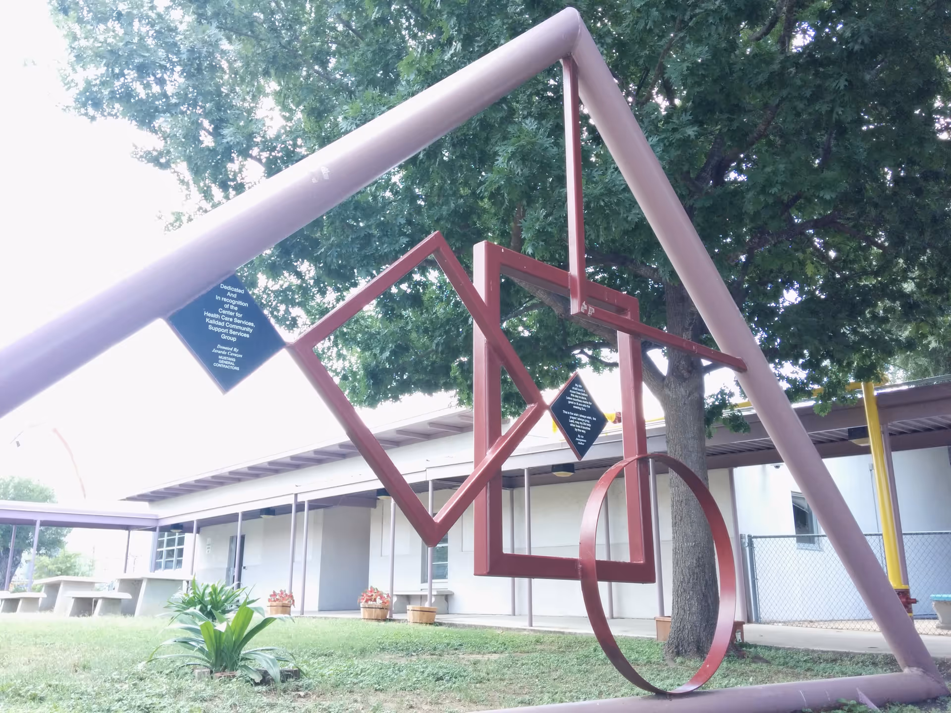 Outdoor geometric metal sculpture installation on a lawn beside a low, long facility building.