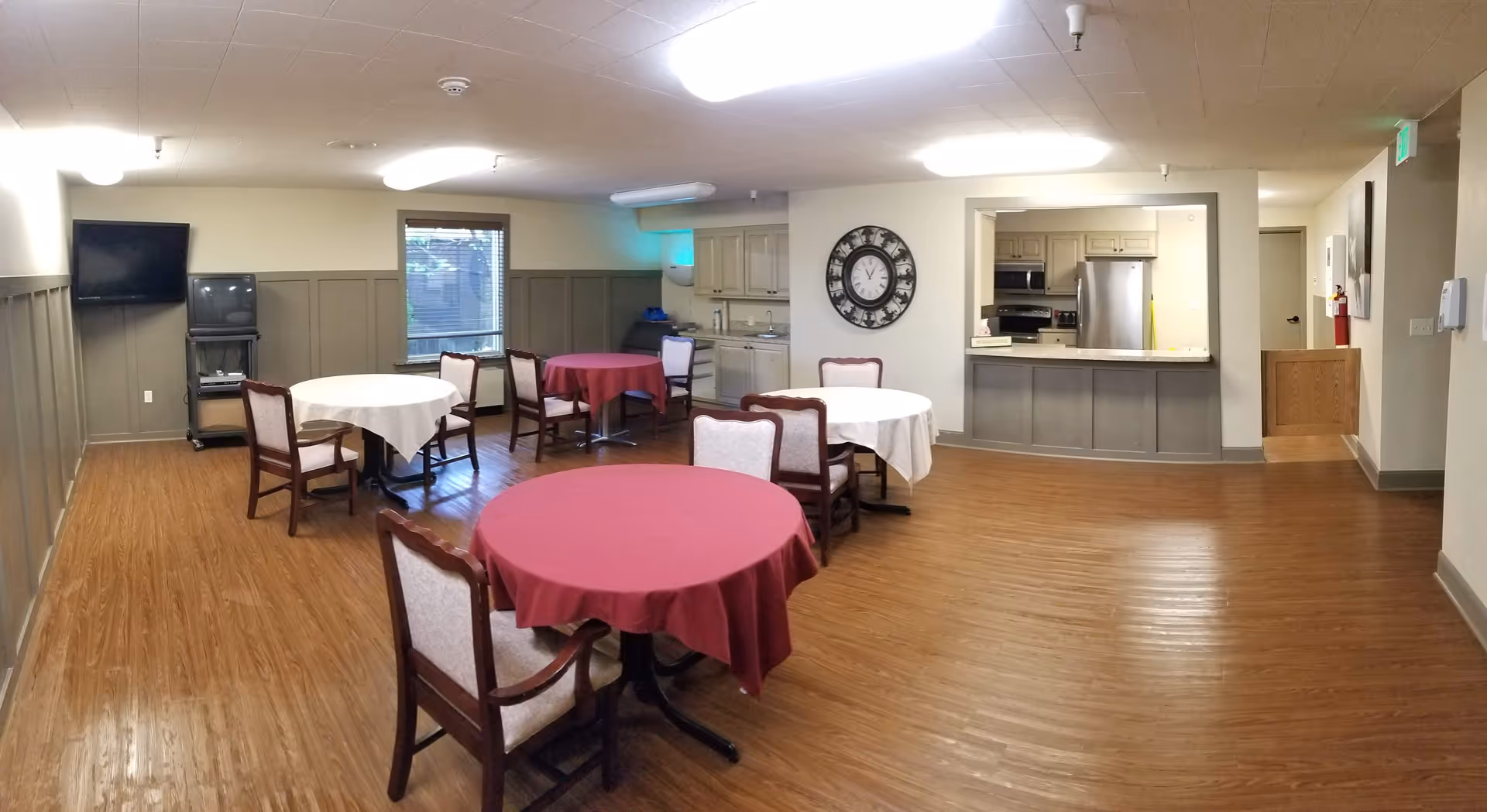 Round tables with red and white tablecloths fill a communal dining area.