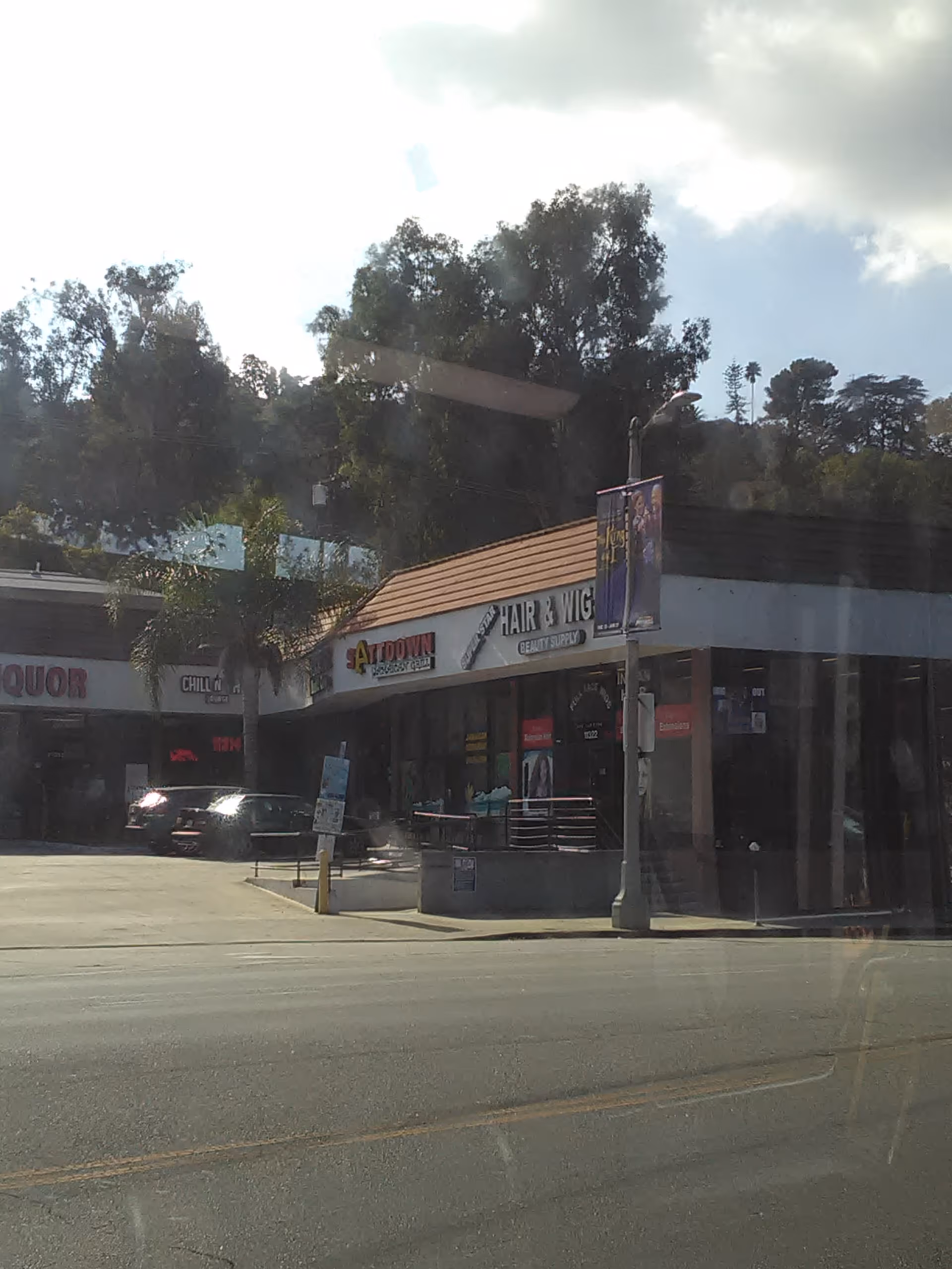 Street-level view of a shopping plaza with storefronts and parked cars.