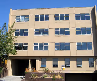 Three-story beige building with many windows and a small entrance area.