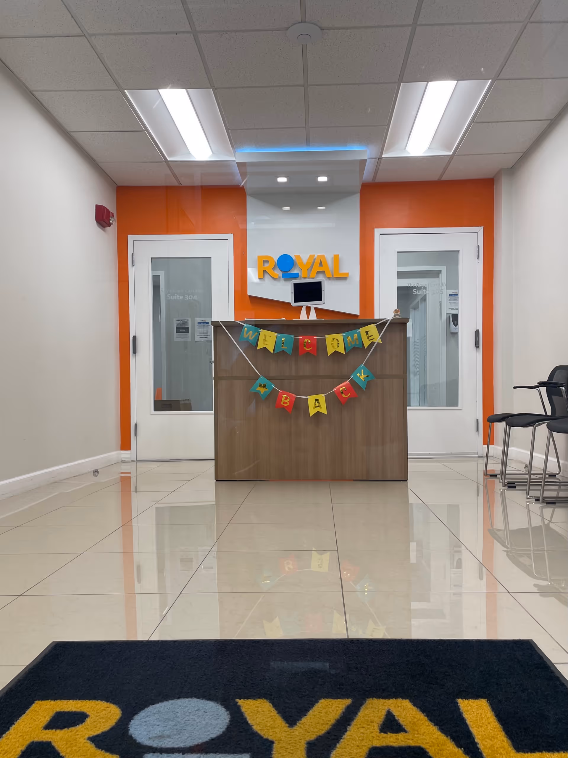 Interior lobby reception at Royal Care with desk, orange accent wall, and welcome banner.
