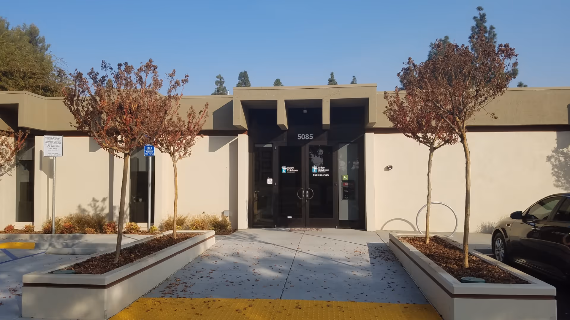 Exterior view of a building entrance with glass doors and planters along the walkway.