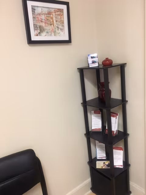 Corner of a beige-walled room with a black shelving unit and framed art