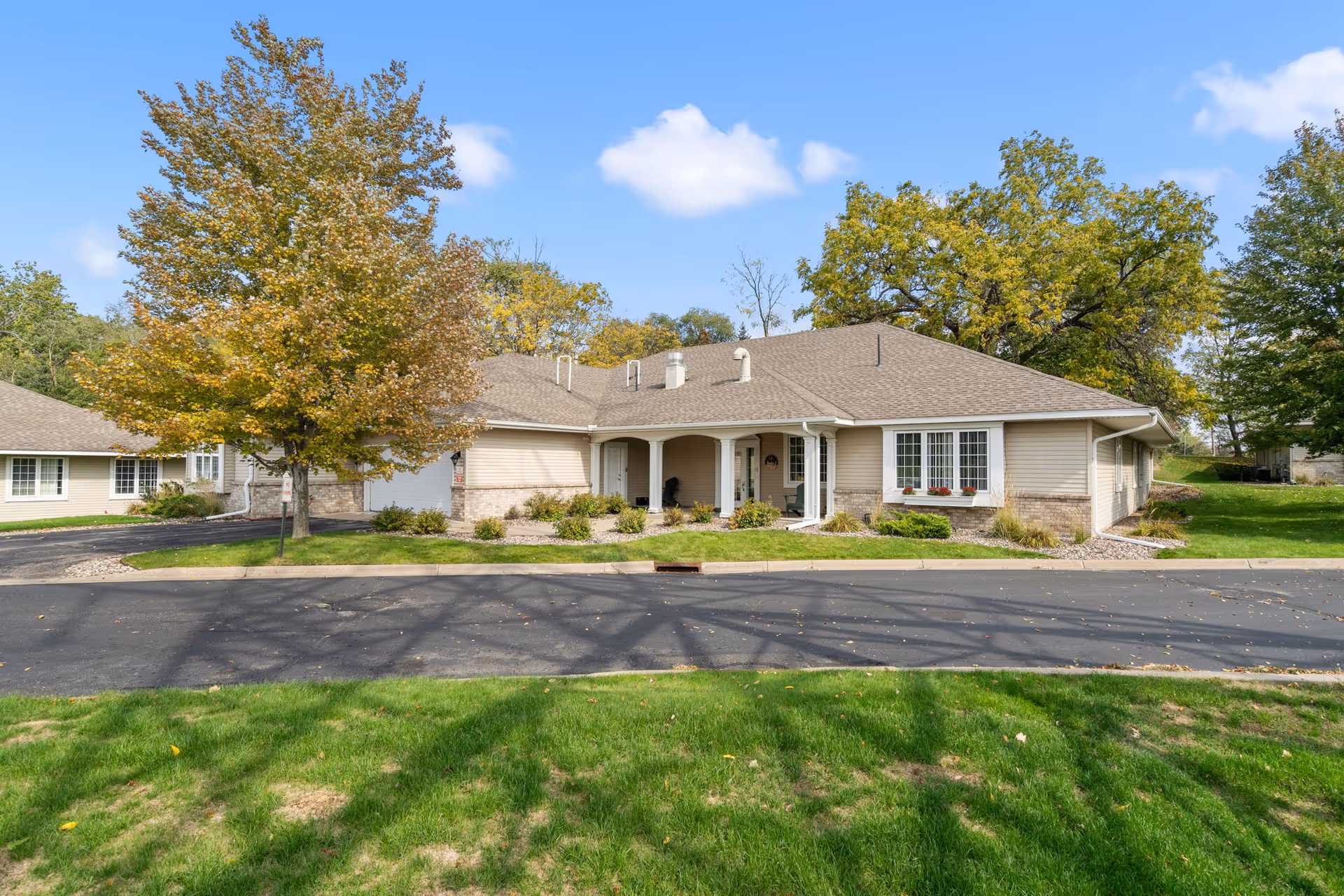 Single-story beige senior living facility with curved entrance, lawn and trees.