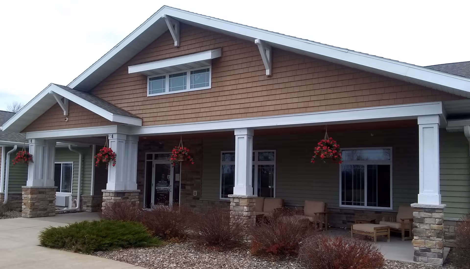 Front exterior of a senior living facility with a covered entrance and hanging flower baskets.