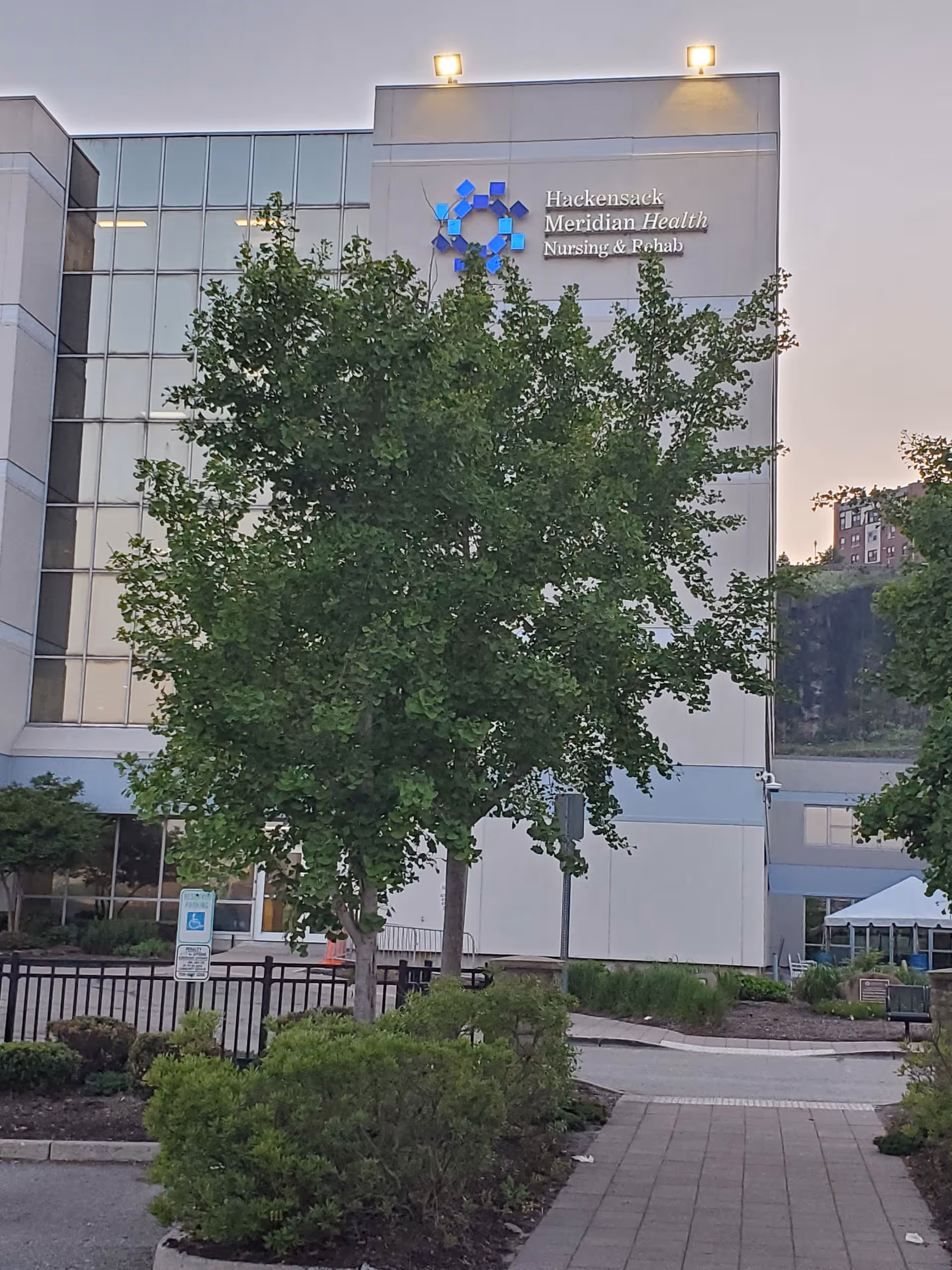 Exterior of Harborage facility with trees, sidewalk, and Hackensack Meridian Health sign.