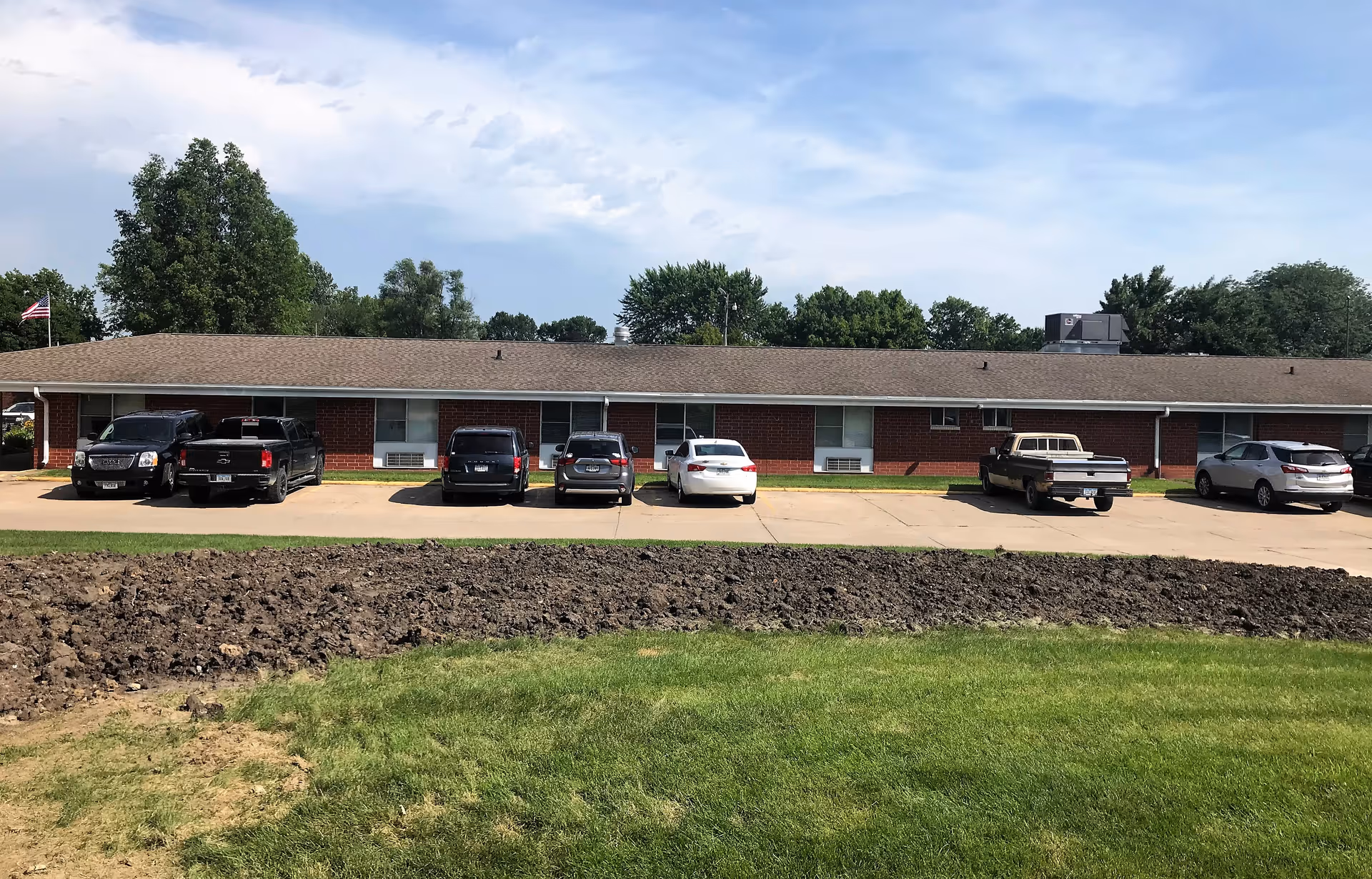 Single-story brick senior care facility with cars parked along the front under a blue sky.