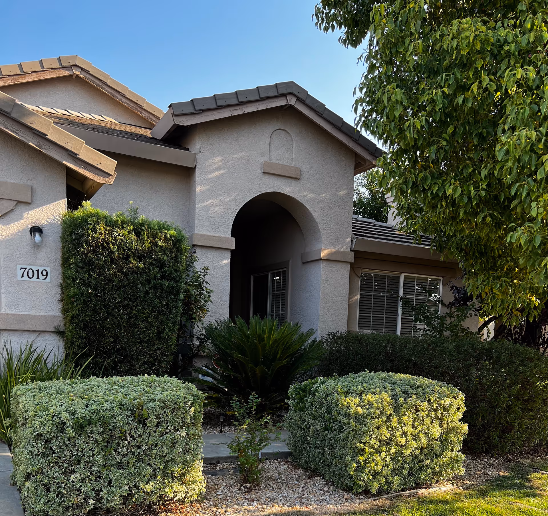 Front entrance of a beige assisted living building with arches and manicured shrubs.