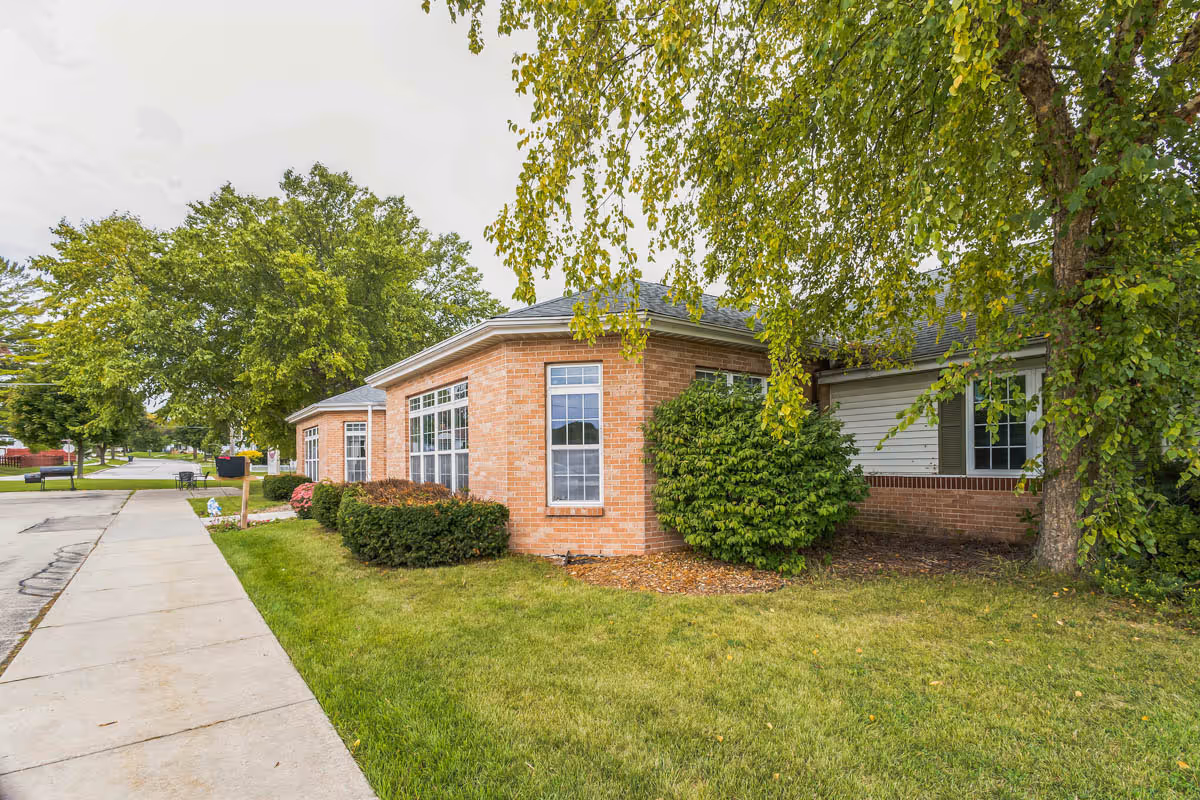 Brick senior living facility with windows, trees, and a sidewalk along a manicured lawn.