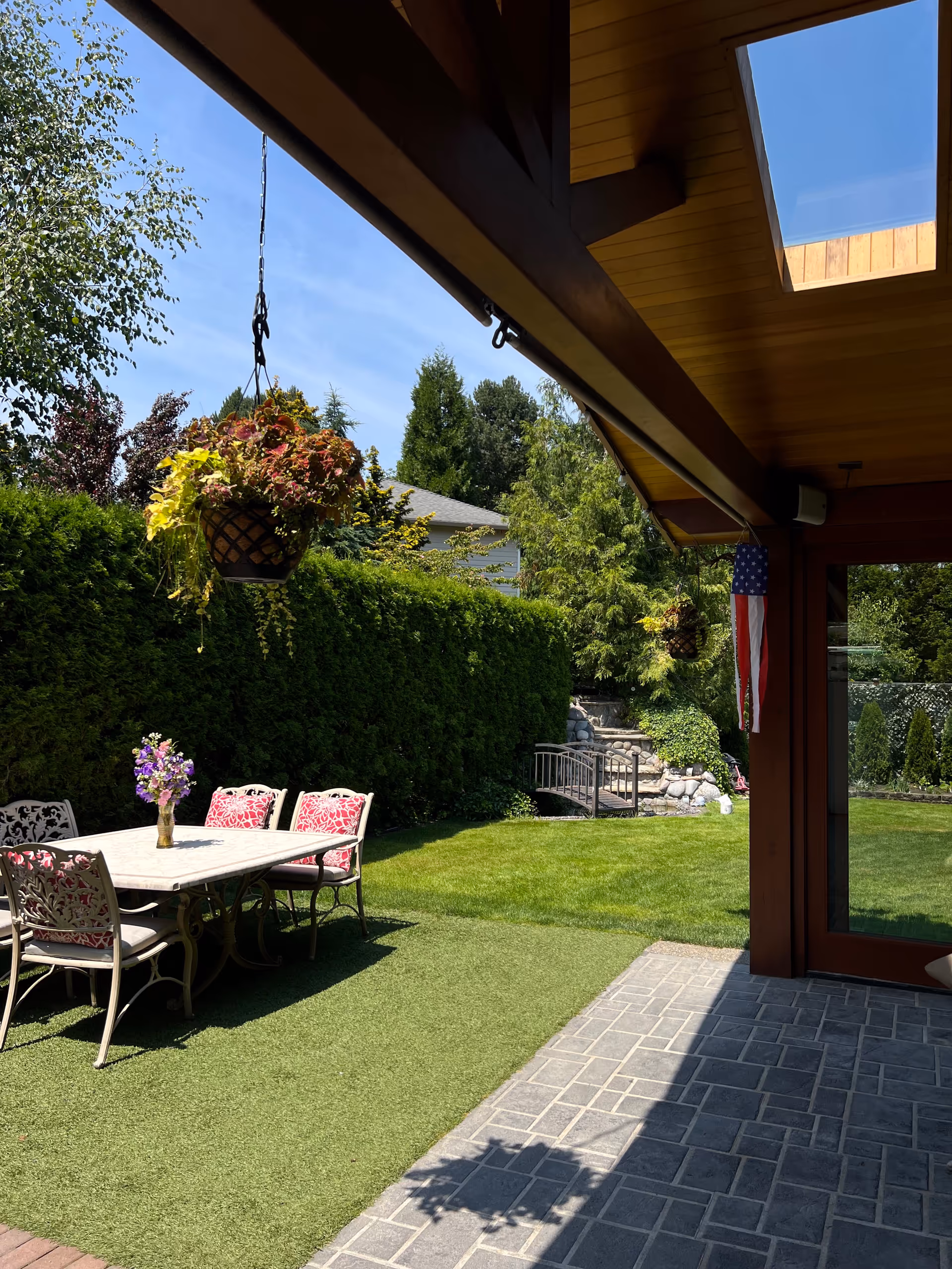 Outdoor patio with a table, chairs, hanging planter, and lawn.