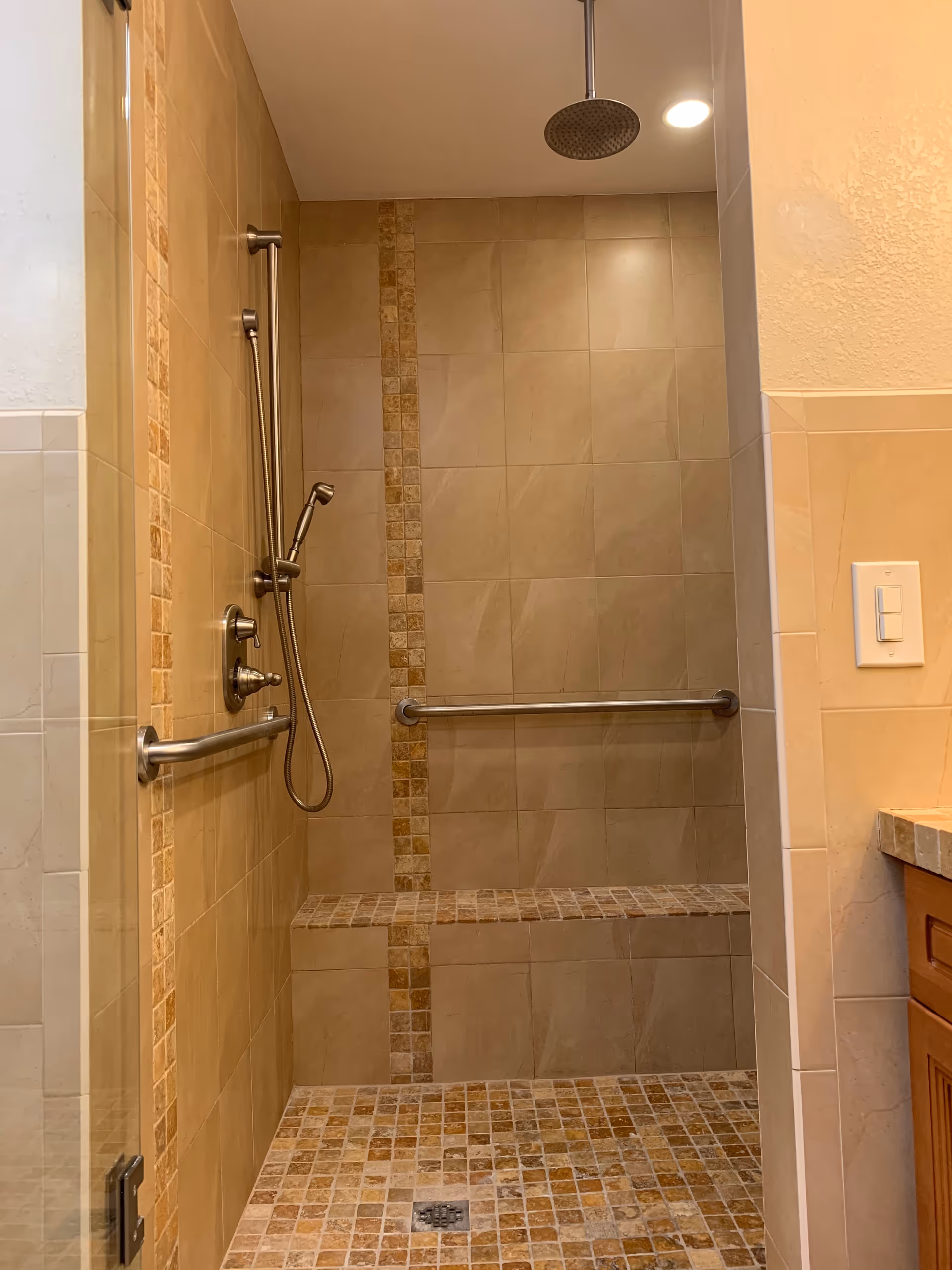 Accessible walk-in shower with bench, grab bars, and tiled walls in a bathroom.