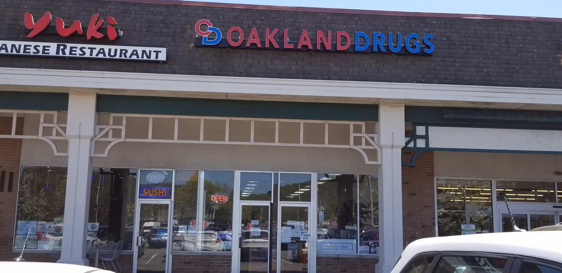 Front view of a strip mall showing Oakland Drugs and Yuki Japanese Restaurant signage.